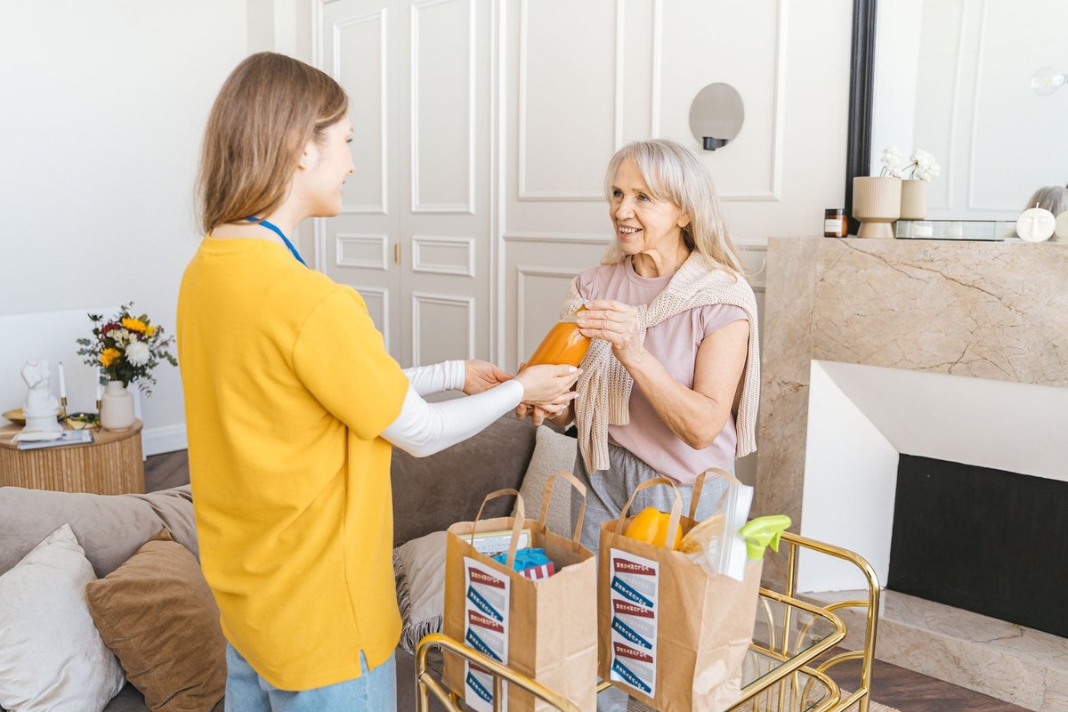 Younger woman handing an orange to an older woman beside paper grocery bags
