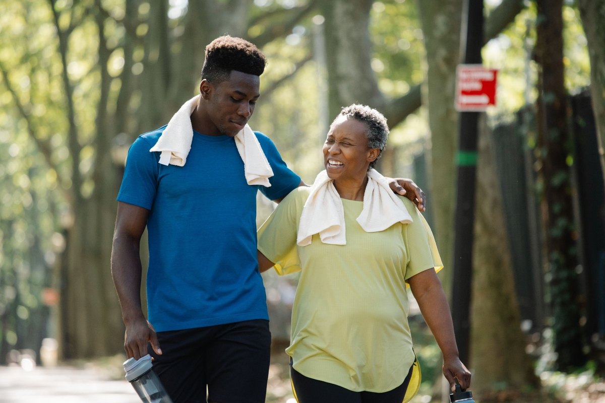 Older woman and younger man walking arm in arm with towels around their necks on a park path