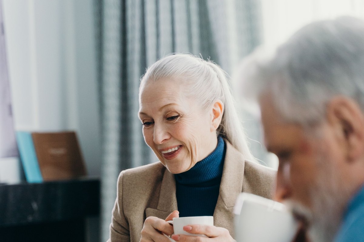 Smiling older woman holding a teacup beside a gray-bearded man drinking from a cup