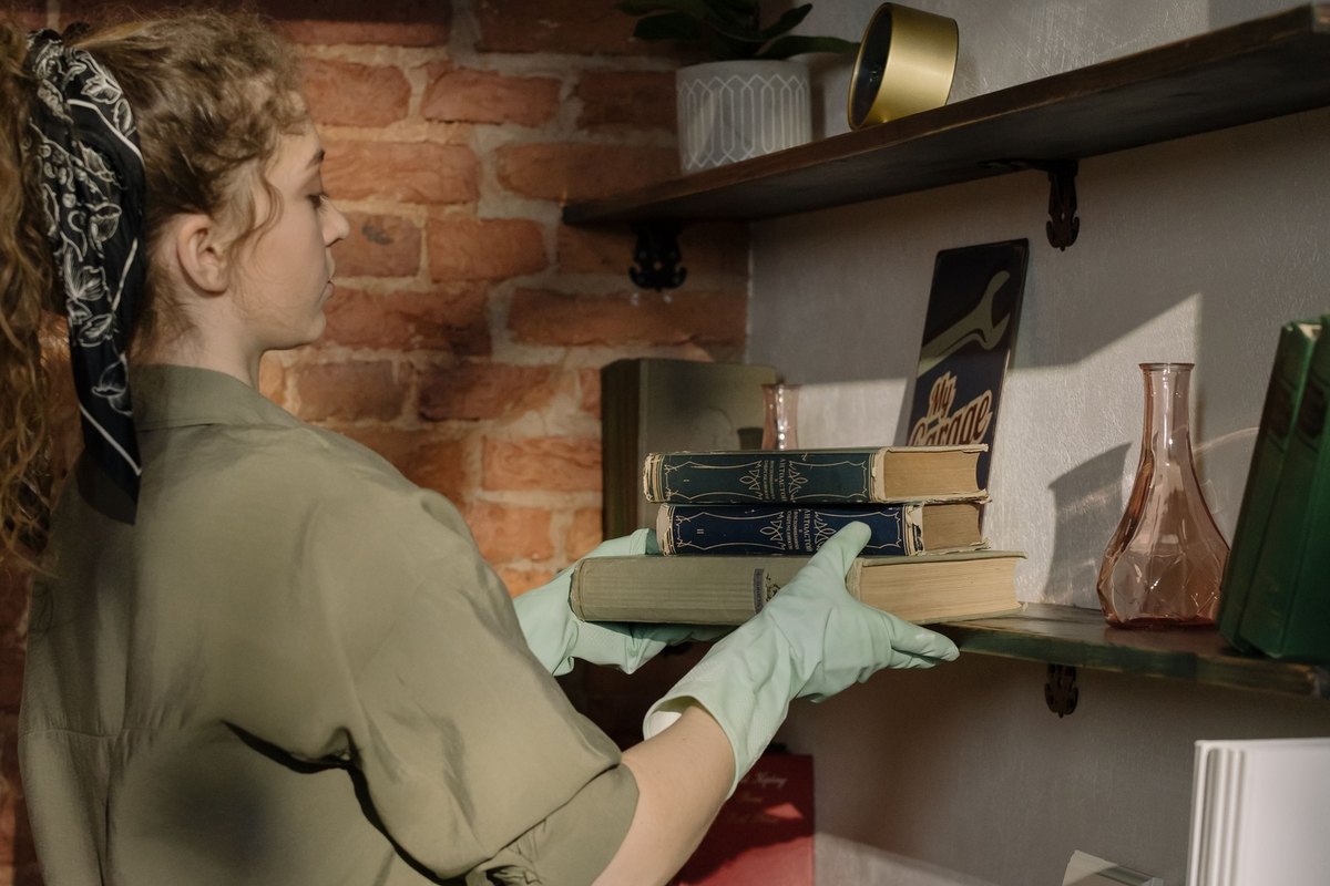 Woman in gloves placing old books on a wooden shelf