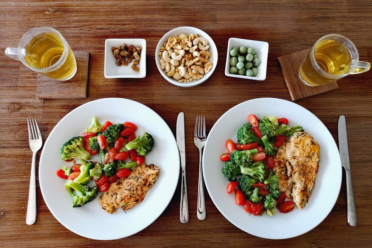 Table set for two with plates of chicken and vegetables and glasses of tea