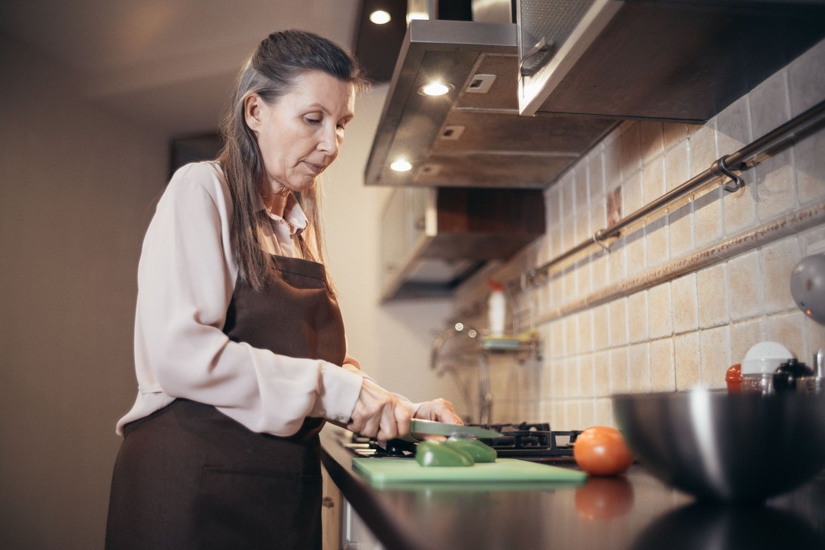 Older woman in an apron cutting green vegetables on a kitchen counter