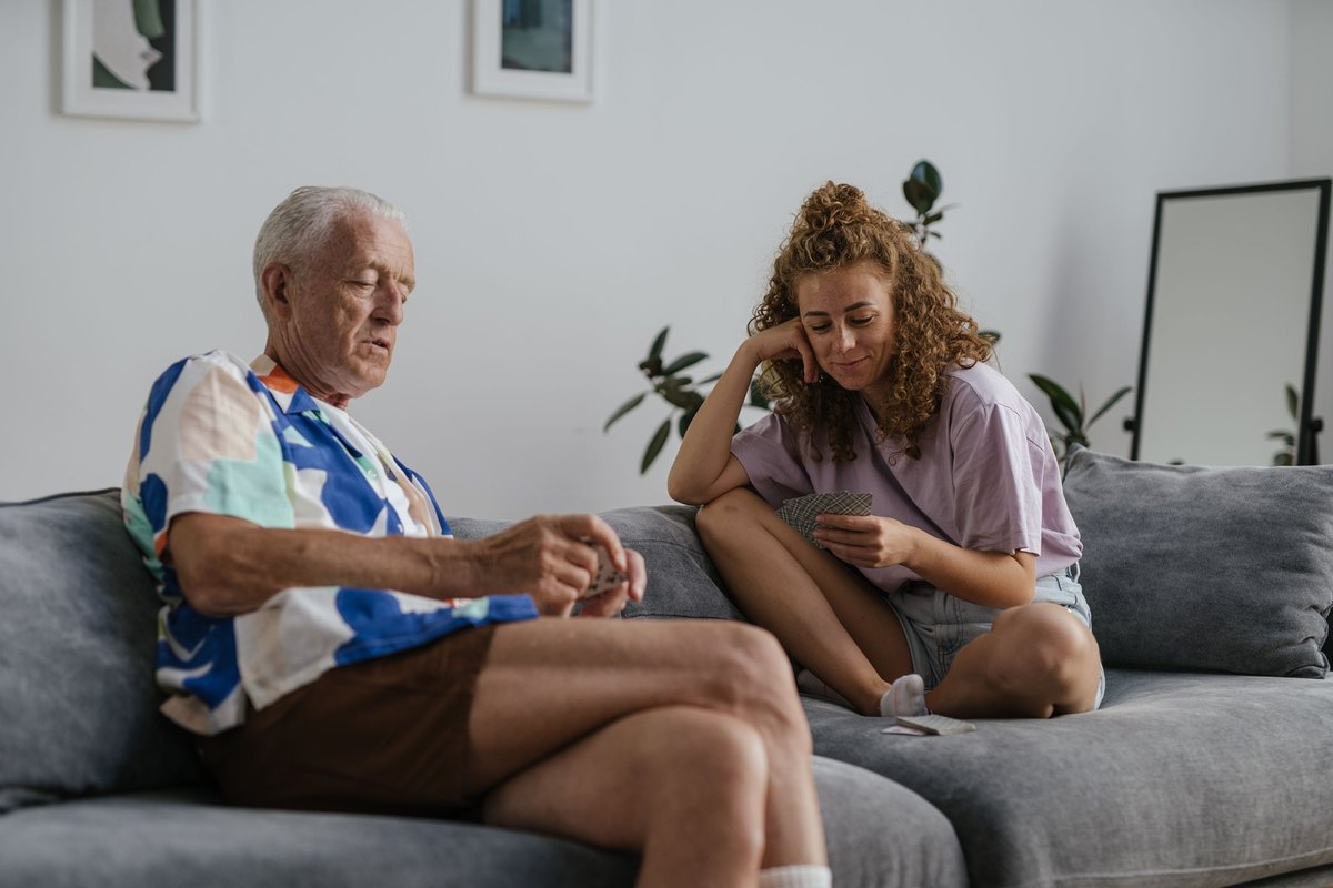 Older man and young woman playing cards on a gray sofa