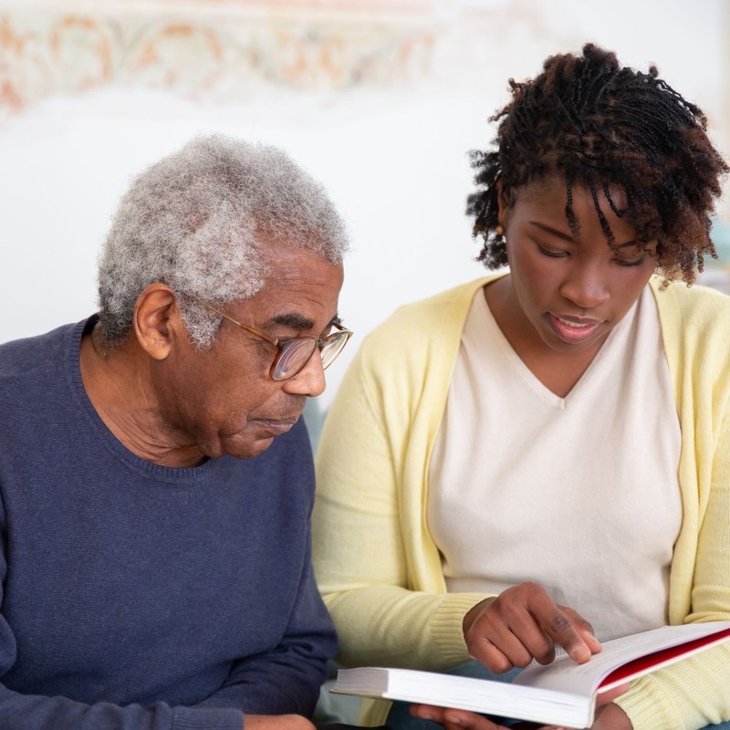 Older man and younger woman reading a book together on a sofa