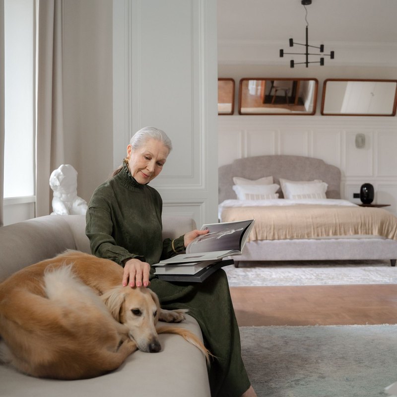 Older woman smiling at a tan dog lying beside her on a gray sofa